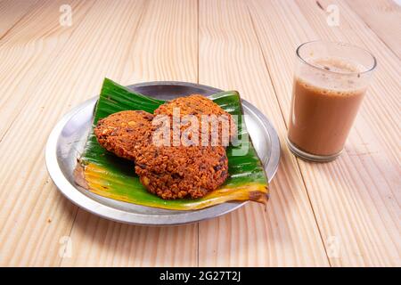 Parippu vada o Lentil Fritters, disposti tradizionalmente in una piastra di acciaio rivestita con foglia di banana e un bicchiere di tè accanto ad esso con legno testurizzato bac Foto Stock