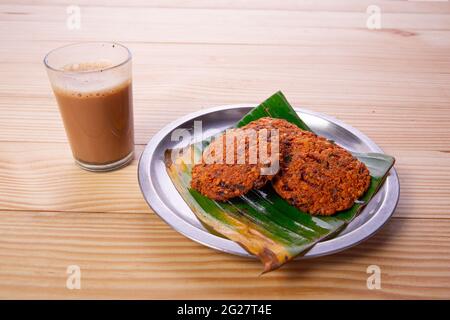 Parippu vada o Lentil Fritters, disposti tradizionalmente in una piastra di acciaio rivestita con foglia di banana e un bicchiere di tè accanto ad esso con legno testurizzato bac Foto Stock