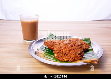 Parippu vada o Lentil Fritters, disposti tradizionalmente in una piastra di acciaio rivestita con foglia di banana e un bicchiere di tè accanto ad esso con legno testurizzato bac Foto Stock