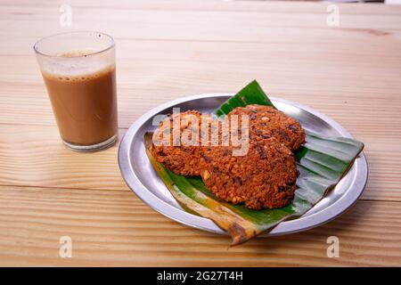 Parippu vada o Lentil Fritters, disposti tradizionalmente in una piastra di acciaio rivestita con foglia di banana e un bicchiere di tè accanto ad esso con legno testurizzato bac Foto Stock