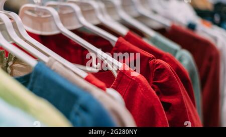 Le t-shirt multicolore in cotone pendono su appendiabiti nel negozio. Foto Stock