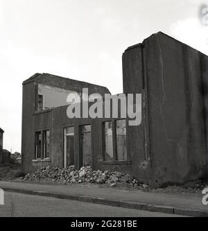 Anni '60 storico, strada e una vista esterna di una coppia di vecchie case a schiera abbandonate, con i tetti e piani superiori andati e con mattoni, vecchie murature e macerie che si trovano a terra, Kelty, Fife, Scozia, Regno Unito. Un villaggio minerario di carbone al confine tra Fife e Perthshire, in quest'epoca, il villaggio si trovava di fronte a un futuro incerto, poiché le miniere di carbone, che un tempo avevano occupato molte centinaia di lavoratori locali dal 1873, quando la prima miniera profonda, la miniera di Lindsey, fu affondata, venivano chiuse o abbandonate. Foto Stock