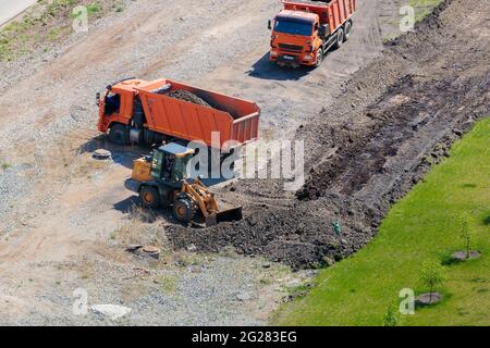 Un operatore su un trattore con una benna carica la terra in un camion. Chelyabinsk, Russia, 15 maggio 2021 Foto Stock