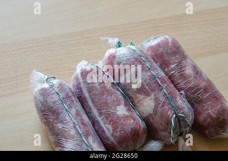 Preparazione graduale del prosciutto tagliato in casa. Fase 13: Quattro rotoli di prosciutto crudo avvolti in pellicola di rivestimento e legati con filo. Pronto per l'ulteriore cottura Foto Stock