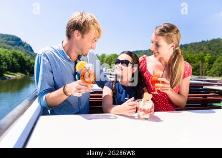 La famiglia felice a pranzo sulla crociera fluviale con bicchieri da birra sul ponte Foto Stock