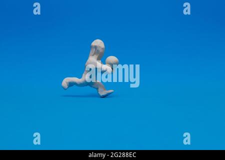 Bambola di plastilina bianca che pratica la pallavolo su sfondo blu. La bambola riceve la palla che la colpisce con gli avambracci. Foto Stock