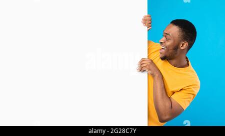 Eccitato Black Man guardando vuoto White Board, sfondo blu Foto Stock