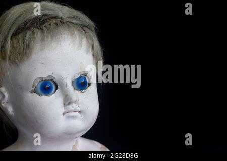 Terrificante e spaventosa vecchia bambola vintage zombie con occhi blu ipnotici su sfondo nero con spazio per la copia. Foto Stock