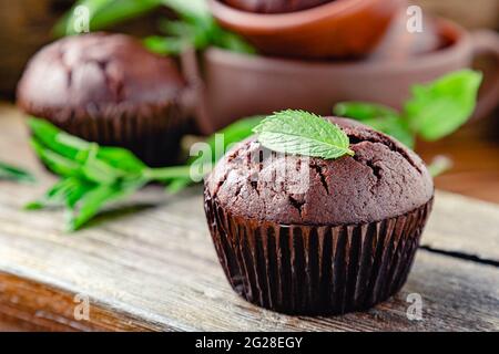 Muffin alla torta al cioccolato con foglie di menta in stile rustico. Muffin al cioccolato appena sfornati senza top su sfondo di legno scuro. Cupcakes con foglia di menta Foto Stock