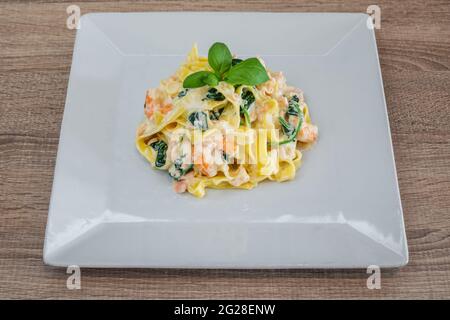 Spaghetti di pasta italiana in salsa cremosa in un piatto di ceramica, con erbe, su un tavolo testurizzato. Con gamberi, vista dall'alto Foto Stock