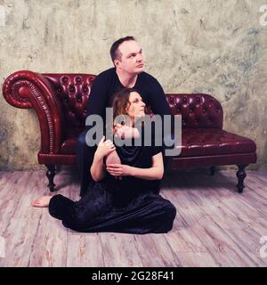 Studio foto di una donna incinta e di un uomo seduto su un divano retrò rosso Foto Stock