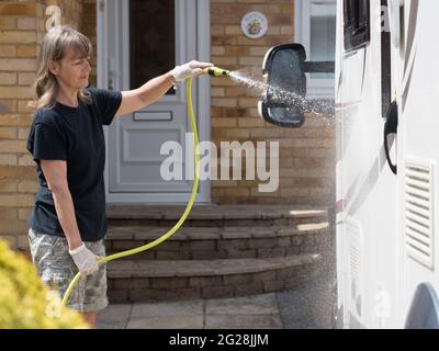 Una signora proprietario del motorhome pulisce il suo veicolo ricreativo con un tubo flessibile pipe.Spray può essere visto che proviene dal tubo come signora pulisce - Foto Stock