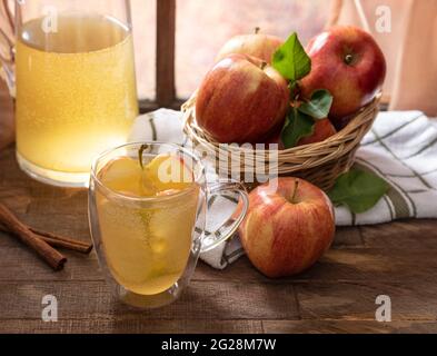 Bicchiere di succo di mela con mele fresche e caraffa su un rustico tavolo di legno Foto Stock