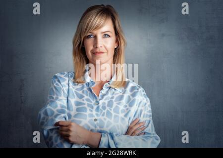Ritratto di attraente donna dai capelli biondi con occhi blu in piedi su sfondo grigio isolato. Spazio di copia. Foto Stock