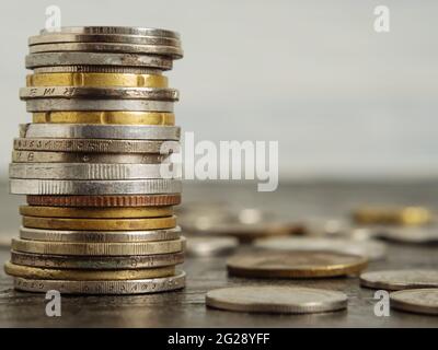 Le monete di paesi diversi sono impilate l'una sull'altra sotto forma di torre. Altre monete sono sparse nelle vicinanze su sfondo nero. Il conc Foto Stock