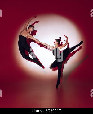 Ballerini balletti che ballano su sfondo rosso dello studio. Design moderno. Luce concettuale colorata e contemporanea come sole nascente al Giappone. Foto Stock