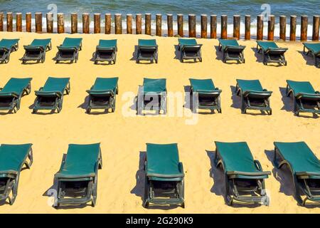 File di lettini verdi gratuiti su una spiaggia di sabbia vuota. Concetto di vacanza chiusa o bassa stagione Foto Stock
