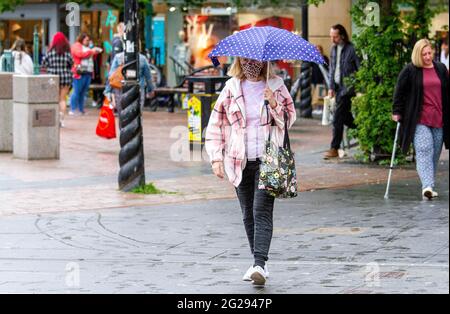 Dundee, Tayside, Scozia, Regno Unito. 9 Giugno 2021. UK Weather: Un giorno coperto e umido con occasionali docce leggere in tutta la Scozia nord-orientale con temperature che raggiungono i 20°C. Le restrizioni di blocco di Covid-19 si sono attenuate a Dundee con persone ancora ben consapevoli delle linee guida di allontanamento sociale e l'uso di maschere facciali. Una donna alla moda prende la giornata per godersi la sua libertà di shopping mentre si ripara dalla pioggia sotto la sua brola nel centro della città. Credit: Dundee Photographics/Alamy Live News Foto Stock