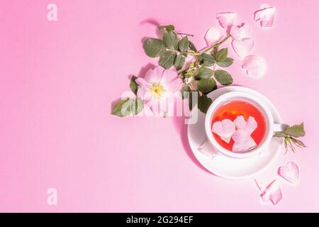 Tè da fiori di rosa fianchi. Bevanda vitaminica estiva, luce dura, ombra scura. Sfondo rosa pastello, vista dall'alto Foto Stock