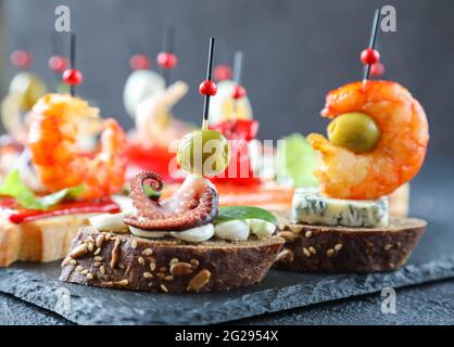 Tapas spagnole creative e sandwich di pesce con polpo, olive su una fetta di pane di sesamo con foglie di basilico e formaggio cremoso per una dieta sana Foto Stock