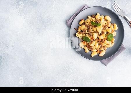 Pasta stufata con manzo e verdure tritate, maccheroni in stile Navy su un piatto. Fondo in cemento grigio. Spazio di copia Foto Stock