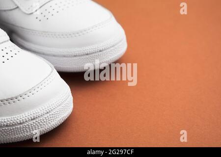 Parte di un paio di eleganti sneaker casual bianche femminili su sfondo marrone Foto Stock