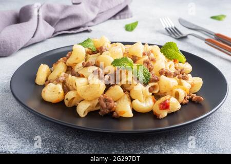 Pasta stufata con manzo e verdure tritate, maccheroni in stile Navy su un piatto. Fondo in cemento grigio Foto Stock