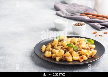 Pasta stufata con manzo e verdure tritate, maccheroni in stile Navy su un piatto. Fondo in cemento grigio. Spazio di copia Foto Stock