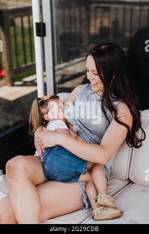 La madre nutre il bambino fuori sul loro portico posteriore in una giornata estiva Foto Stock