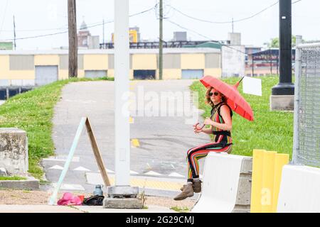 NEW ORLEANS, LA, Stati Uniti d'America - 9 MAGGIO 2021: Donna in costume colorato pant siede su barricata di cemento che tiene un ombrello Foto Stock