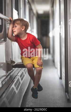 il bambino annoiato che guarda fuori dalla finestra sul treno Foto Stock