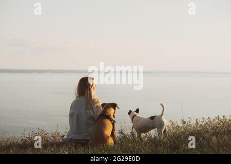 Donna godendo il tramonto dal grande lago o baia con i suoi cani Foto Stock