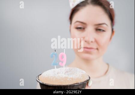 La donna felice fa un desiderio e soffia fuori le candele sulla torta di compleanno 29. Sorridente ragazza che festeggia il compleanno. Foto Stock