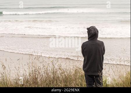 Uomo solitario in una cappa in posizione sulla spiaggia Foto Stock