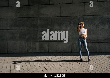 Foto d'inventario di ritratto di giovane ragazza bionda riccia contro il muro. Ha un atteggiamento fiducioso. Indossa abiti casual Foto Stock