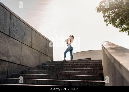 Foto d'inventario di ritratto di giovane bionda curly ragazza che danzano per strada. Indossa abiti casual Foto Stock