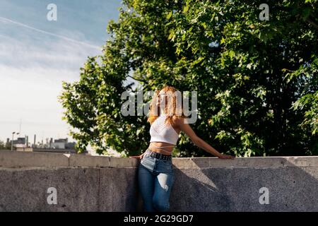 Foto d'inventario di ritratto di giovane ragazza bionda riccia contro il muro. Ha un atteggiamento fiducioso. Indossa abiti casual Foto Stock