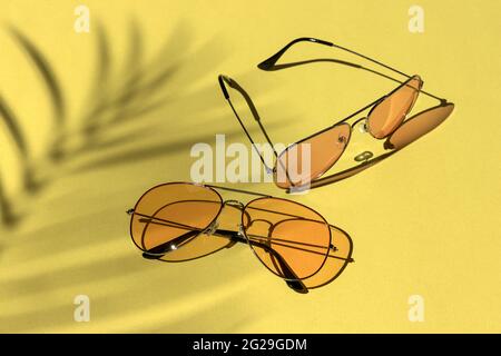 occhiali da sole gialli sotto una palma su uno sfondo luminoso. ombre dure dal sole a mezzogiorno. concetto di svago, viaggio e intrattenimento con copy spa Foto Stock