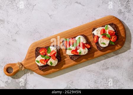 Sandwich di pane integrale con formaggio, pomodori e foglie di basilico, vista dall'alto. Concetto di snack sano. Foto Stock