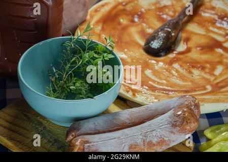 Ingredienti culinari per preparare la pizza fatta in casa. Prezzemolo, rosmarino, erba cipollina, peperoni e salsa di pomodoro. Pasta per pizza con salsa rossa e condimenti. Foto Stock
