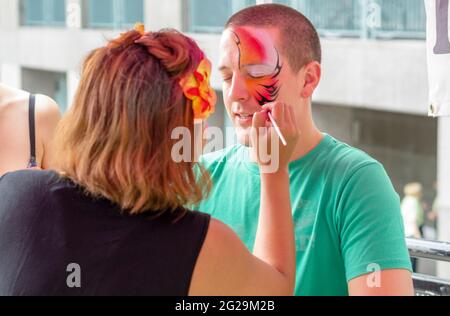 Ispanic Fiesta: Donna bionda che applica il facepaint colorato all'uomo che indossa la camicia verde, l'uomo con gli occhi chiuso.August 31, 2013 a Toronto, Canada Asu Foto Stock