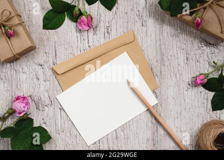 Confezione regalo avvolta con carta kraft e fiori rosa su tavolo grigio. Foglio di carta vuoto per il testo. Vista dall'alto. Disposizione piatta. Spazio di copia Foto Stock