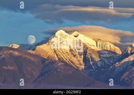 Luna che si erge sulle cime innevate della Mission Mountain Range nel Montana occidentale, NON è stata fotografata Foto Stock