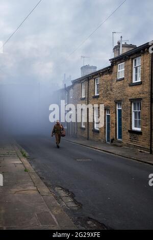 Un soldato della seconda guerra mondiale cammina su una strada degli anni '40 che rappresenta Manchester nelle riprese del Railway Children Return girato su Herbert Street Saltaire Foto Stock