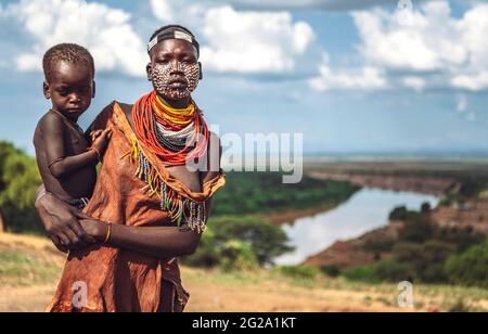 Giovane donna con faccia dipinta che tiene il suo ragazzino nel villaggio della tribù Karo. Valle di Omo, Etiopia; Foto Stock