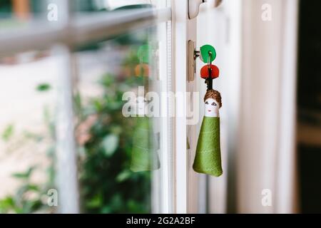 Divertente portachiavi umano a forma triangolare con le chiavi che si stacca dalla serratura della porta trasparente del balcone dell'appartamento moderno Foto Stock