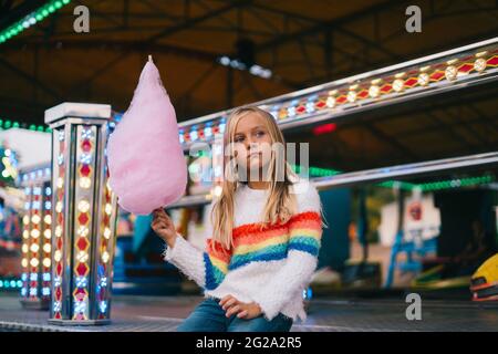 Ragazza carina piccola che tiene una caramella di cotone mentre attende il suo turno alle auto d'urto Foto Stock