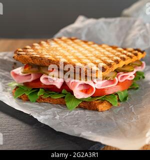 Delizioso sandwich con rucola, pomodori e cetrioli. Fette sottili di prosciutto fresco. Uno spuntino veloce. Messa a fuoco selettiva. Foto Stock