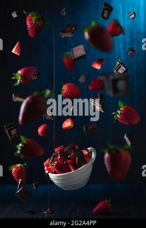 Tazza volante con fragole e pezzi di cioccolato su sfondo blu Foto Stock