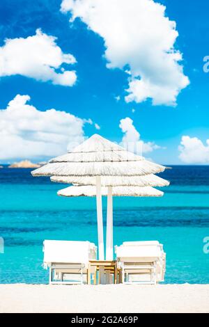 (Fuoco selettivo) splendida vista di alcuni ombrelloni e lettini di paglia bianca su una spiaggia di sabbia bianca bagnata da un bel mare turchese. Foto Stock